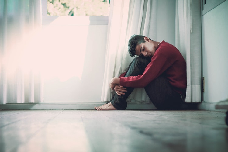 Jeune homme souffrant d'un syndrome de stress post-traumatique assis au coin d'une pièce